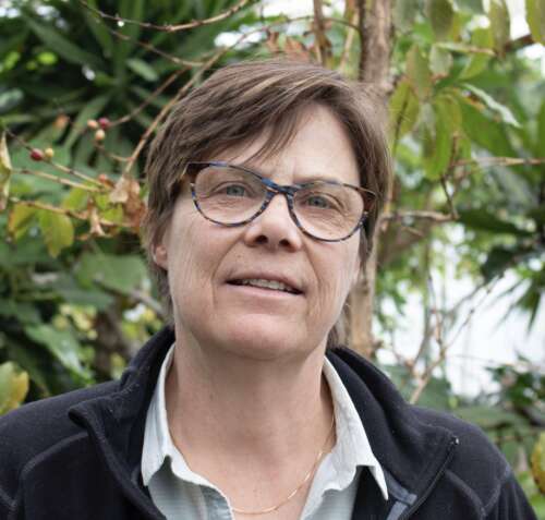 Dr. Jan Sargeant poses for a photo against tropical trees in a greenhouse