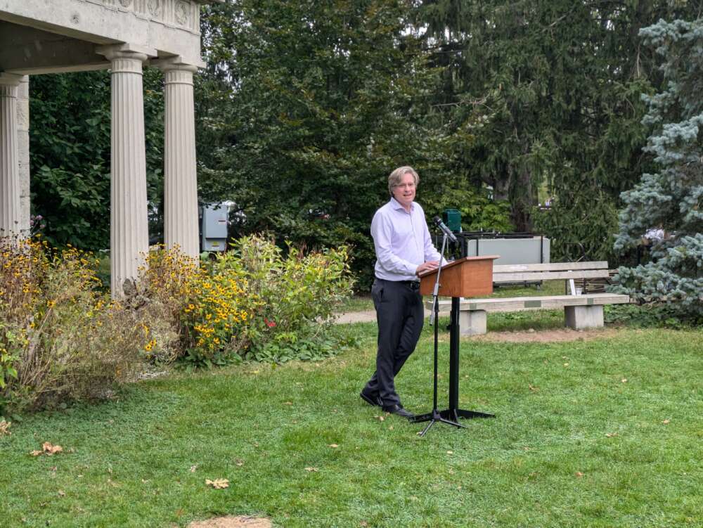 Bill Rosehart stands at a podium and addresses the crowd in front of the portico