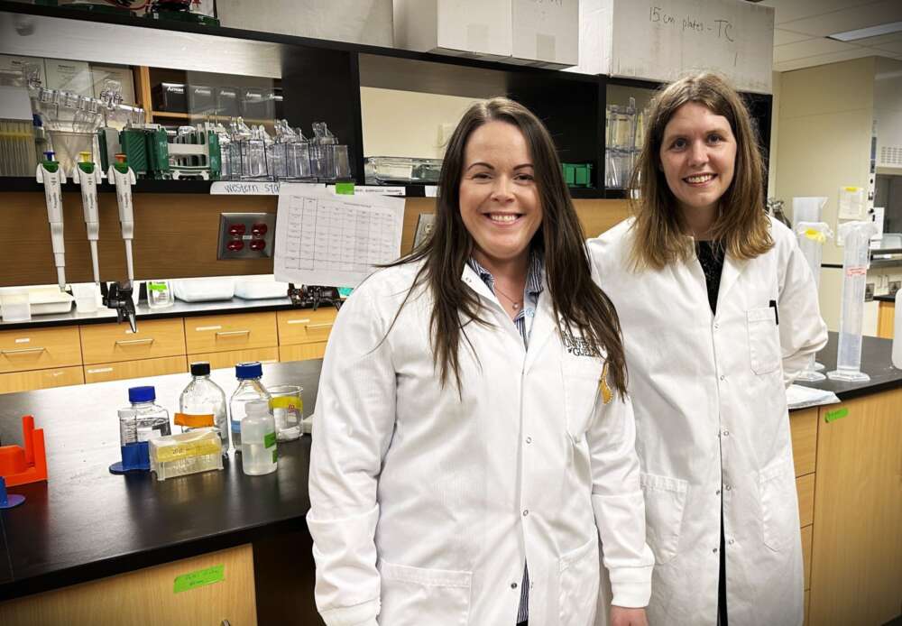 two women in lab coats pose for a photo in a biology lab