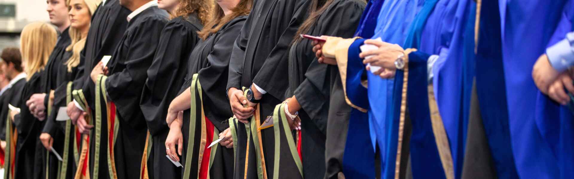 The hands of several graduands in robes