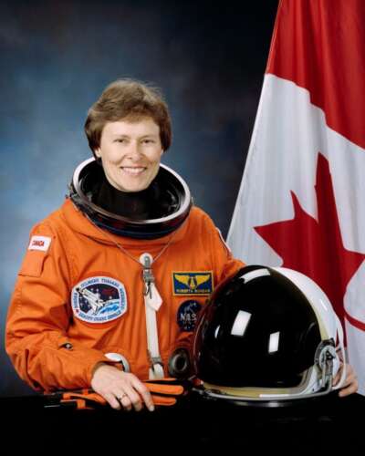 Official portrait of Roberta Bondar wearing her astronaut suit next to a Canadian flag.