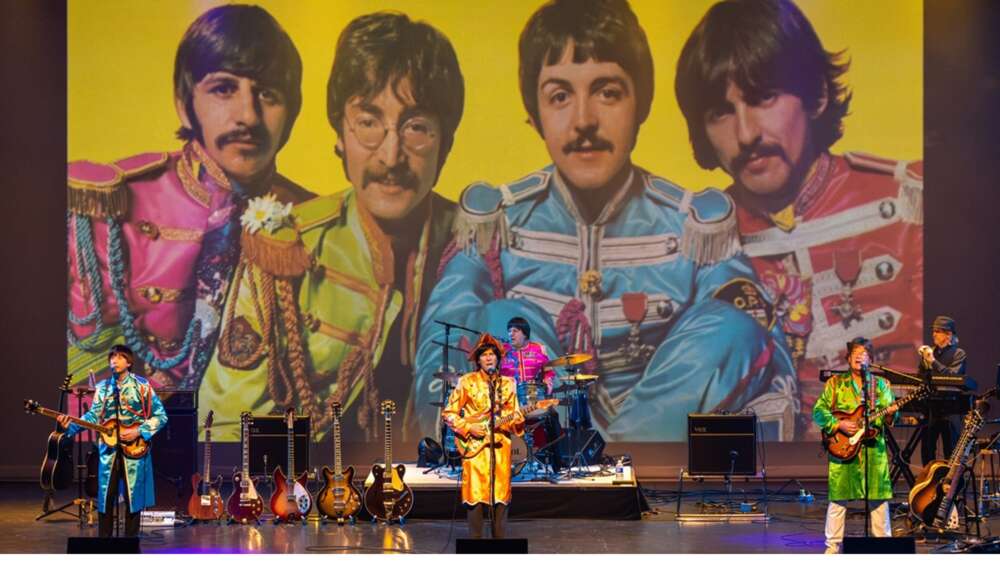 A beatles tribute band plays in front of a large image of the original beatles.