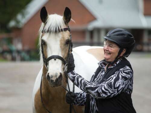 a woman in a riding hat poses beside her horse