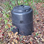 A black plastic compost bin sitting outdoors.