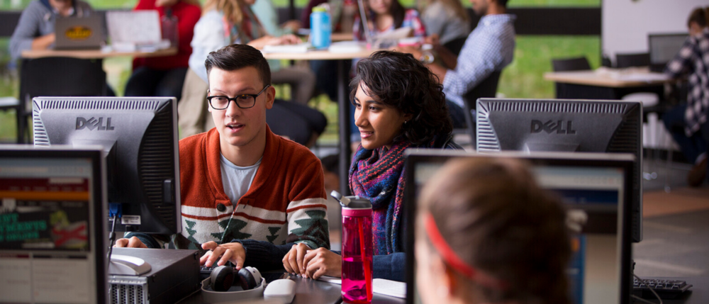Two students in a computer lab, both examining a screen