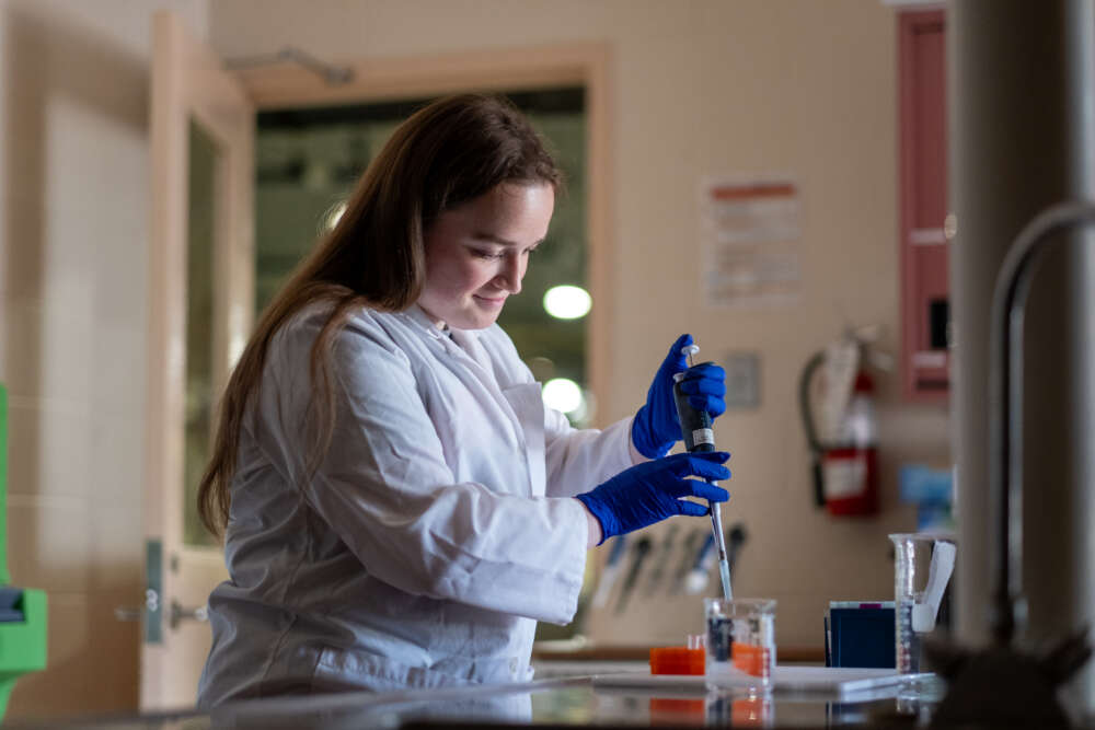 a person in a lab coat uses a large pipette to remove liquid from a vial