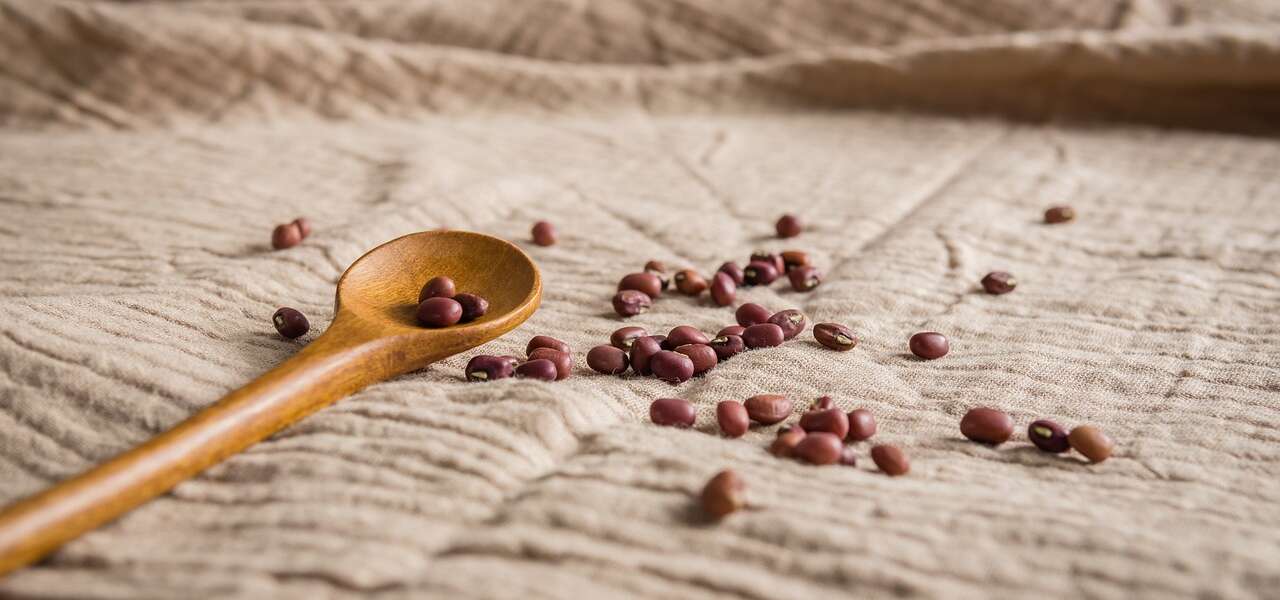 Red kidney beans appear on a woven brown cloth with some spilling from a wooden spoon.