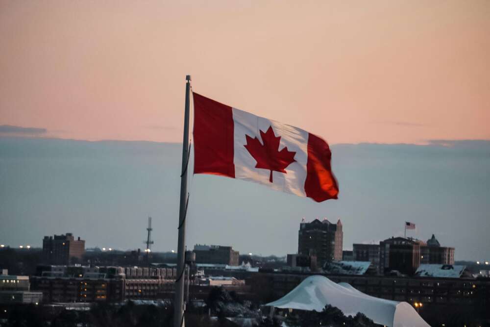 A Canadian flag against an urban background at dusk