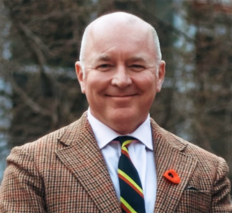 a man in a plaid suit jacket and tie, wearing a red poppy, poses for a headshot