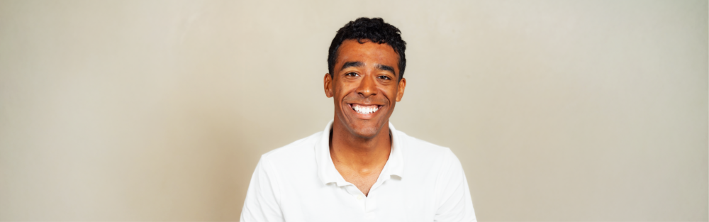 Headshot of Jayden Parker, smiling against a beige studio background. He has short black hair and is wearing a white collared shirt.