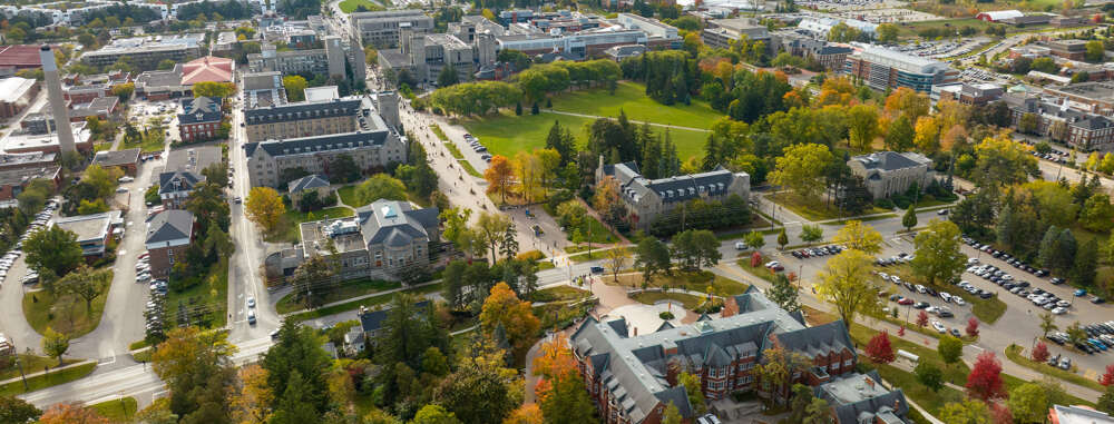An aerial view of the University of Guelph campus depicts multiple buildings among lush trees and Johnston Green.