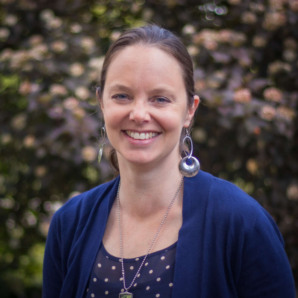 Andrea Paras standing outside, wearing a blue cardigan and blue polka dot top with large earrings.