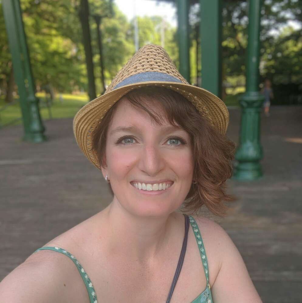 a woman in a green top and a straw hat poses for a photo in front of a green background