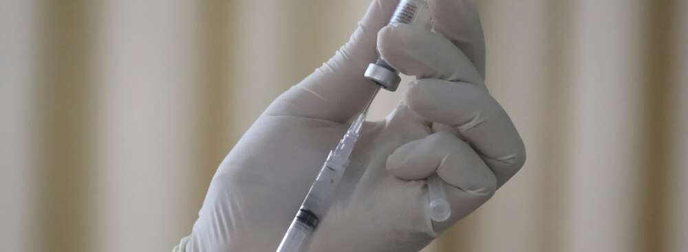 person wearing white gloves drawing vaccine out of a vial