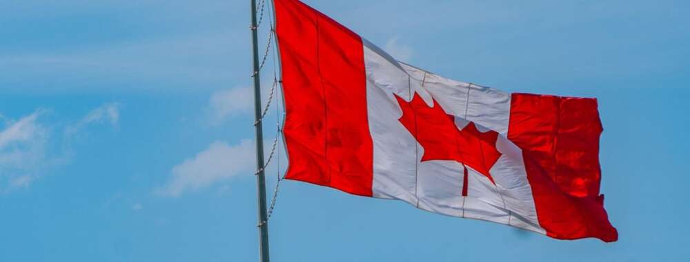 a canadian flag flies in front of a bright blue sky
