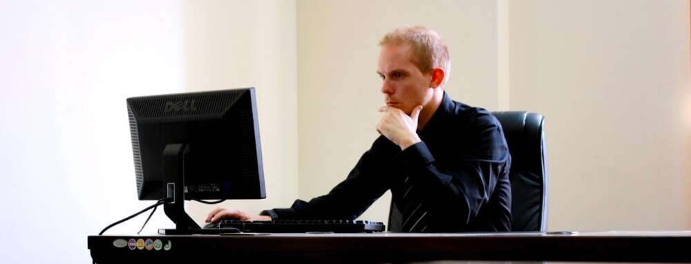 a person rests their chin in their hand while staring at a computer monitor
