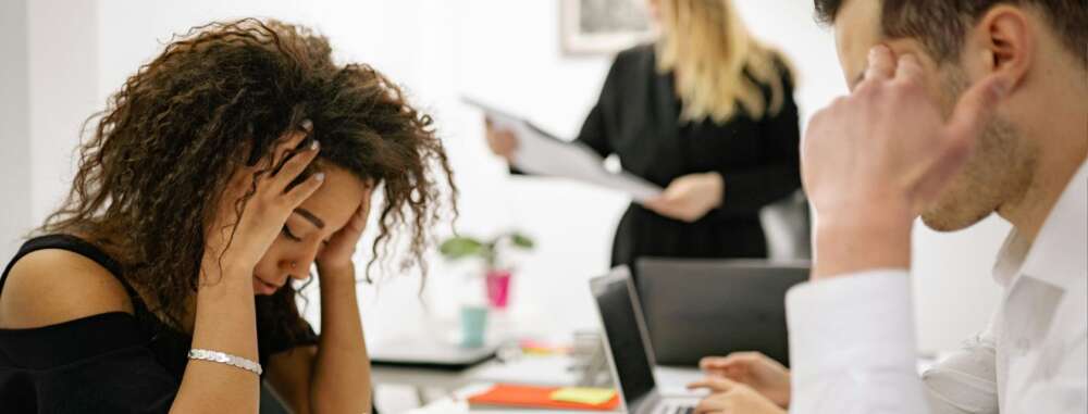 people in an office setting hold their heads in their hands while sitting at a table