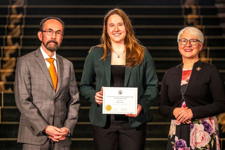 a person holds a plaque with two presenters flanking her