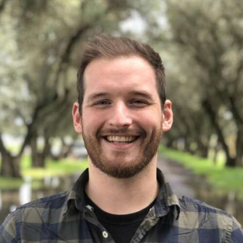 A person with brown hair wearing a plaid shirt poses for a headshot