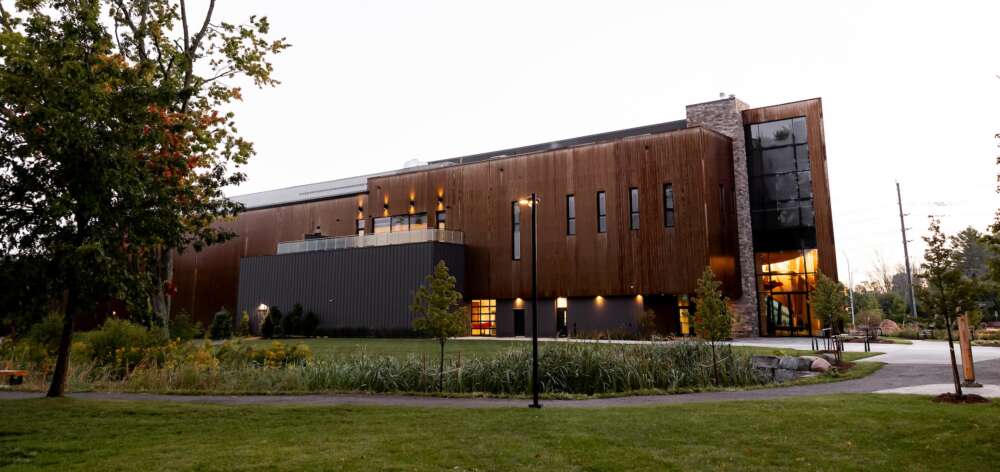 A wooden building sits illuminated at dusk surrounded by landscaping and trees.