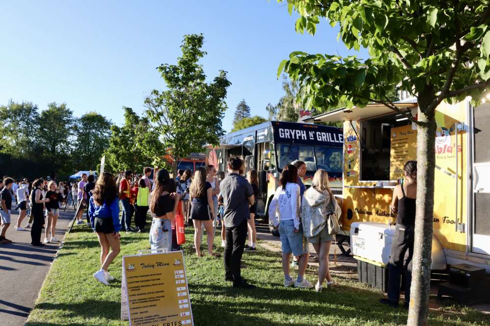 students line up at food trucks on a green lawn