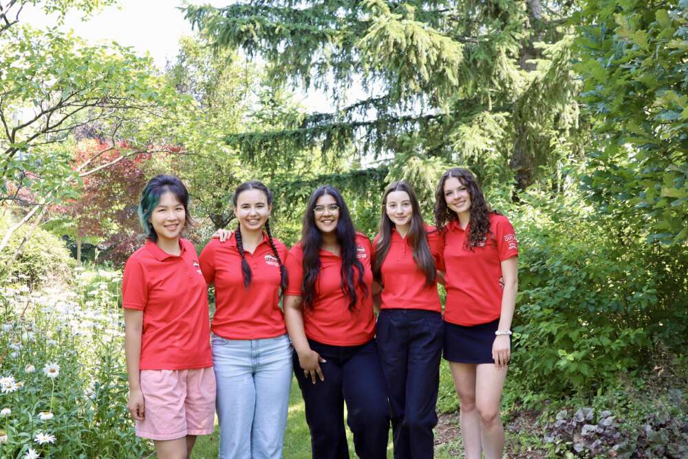 five students in red polo shirts pose for a group photo in front of a green background