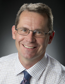 Headshot of Dr. Istvan Rajcan, wearing a checkered button up shirt and smiling.