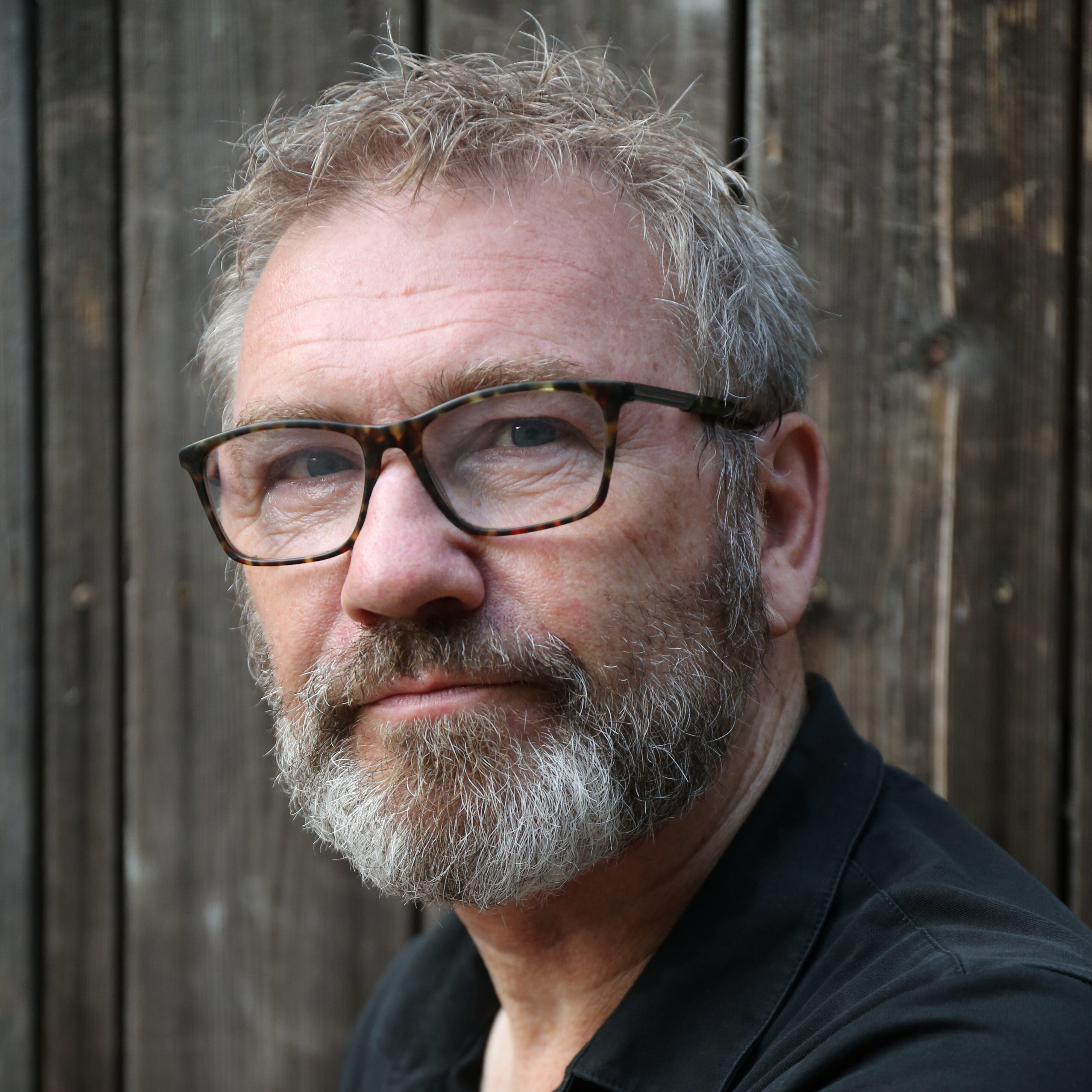a person with short hair and a beard wearing glasses and a black shirt poses for a headshot