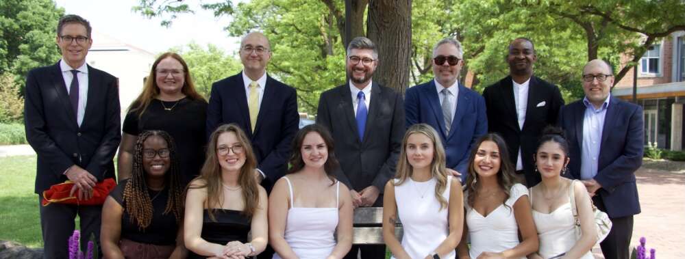 A group of JLS faculty stand in a row behind a row of the program's first graduates sitting on a bench newly installed on the U of G campus.