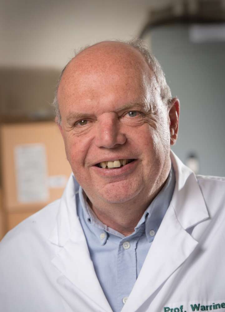 Headshot of Dr. Keith Warriner. He wears a white lab coat with "Prof. Warriner" engraved on the pocket, and a blue dress shirt underneath