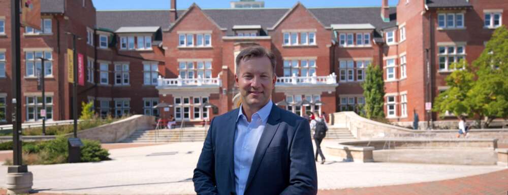 a person in white shirt and navy blue blazer poses in front of a red brick building