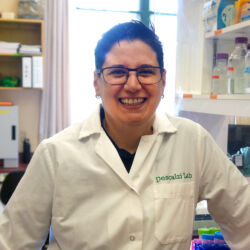 Dr. Giannina Descalzi wears a lab coat and smiles in a lab