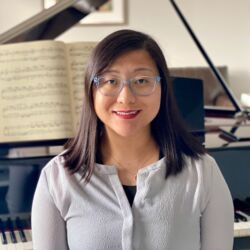 a person poses for a photo in front of a grand piano