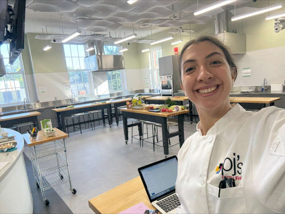 A person in chef's white takes a selfie while in a kitchen class space