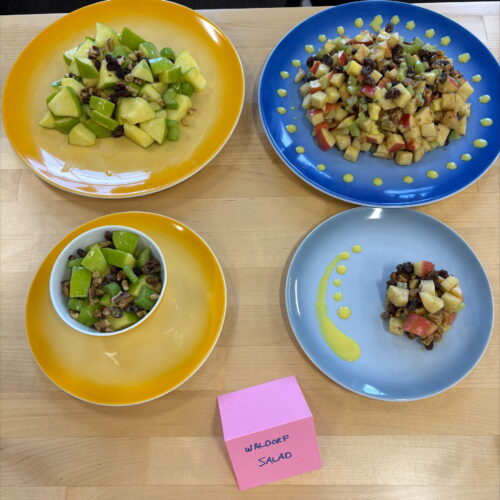 pieces of cut up apples are shown on four yellow and blue plates, sitting on a table with a pink card that reads WALDORF SALAD