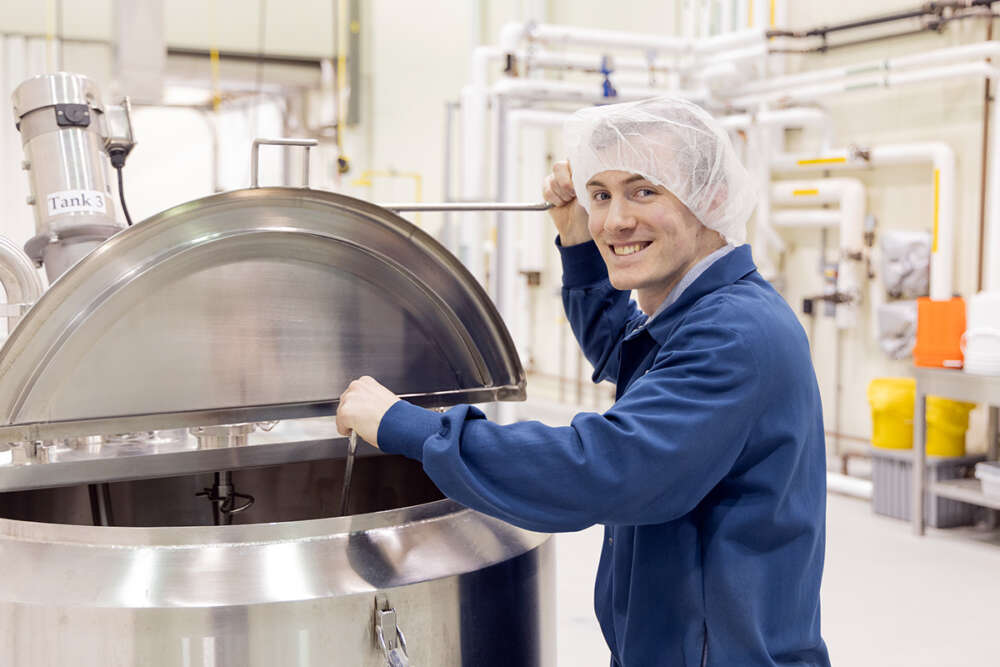 A food science co-op students wears a hairnet and mixes a giant vat in an industrial kitchen
