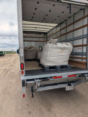 The back of a transport truck is open revealing a giant, white bag of beans on a skid