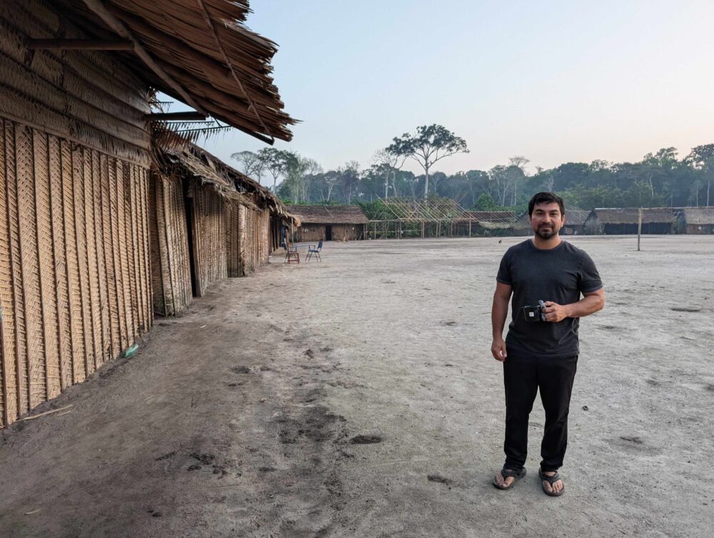 Good stands with mug in sandy village clearing