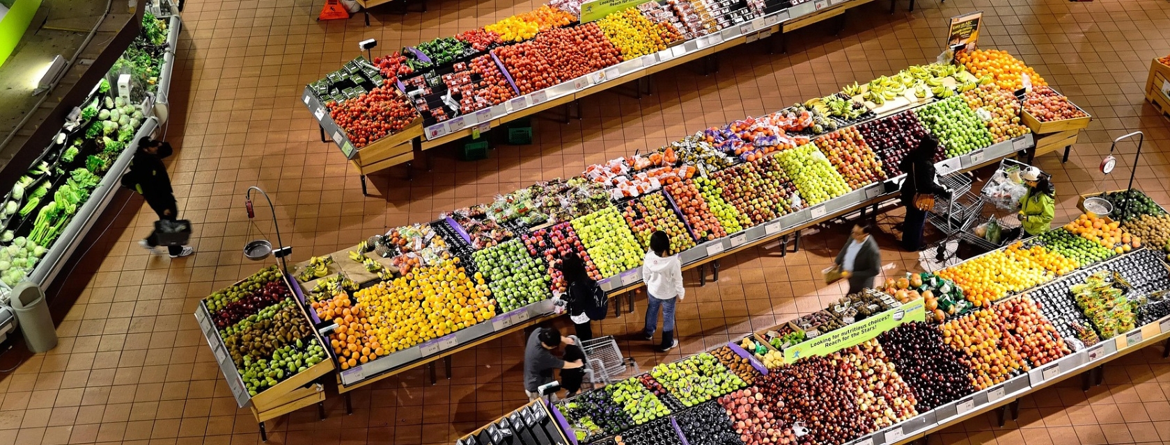 Overhead view of shoppers in produce section filled with fruits and vegetables.