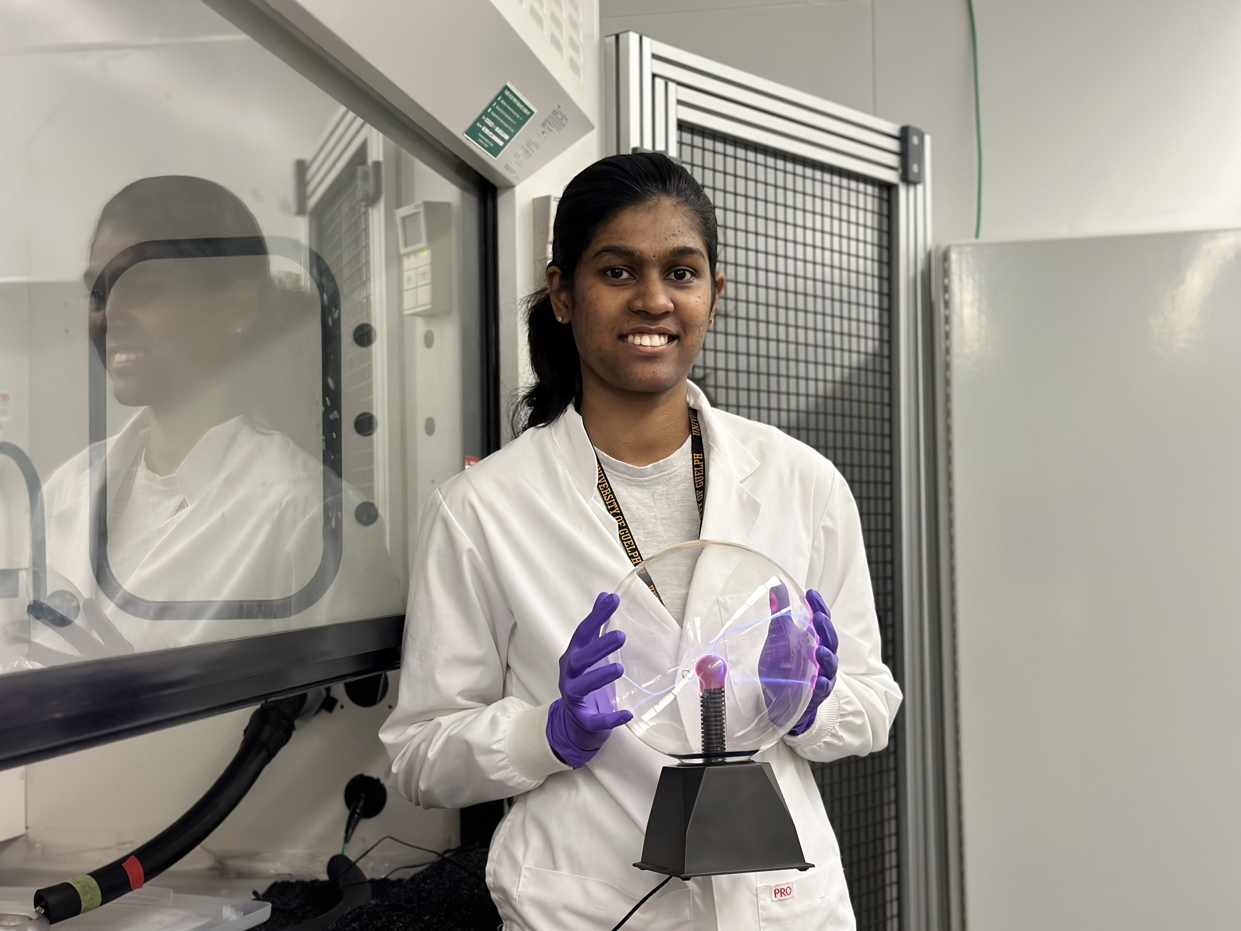 Researcher in lab coat holds plasma globe inside laboratory.