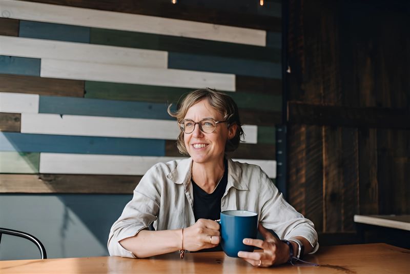 Researcher with short hair and glasses smiles to the side with mug in hand