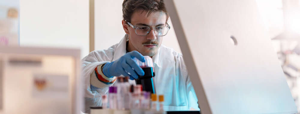 Closeup of a student scientist in lab coat and gloves handling lab equipment