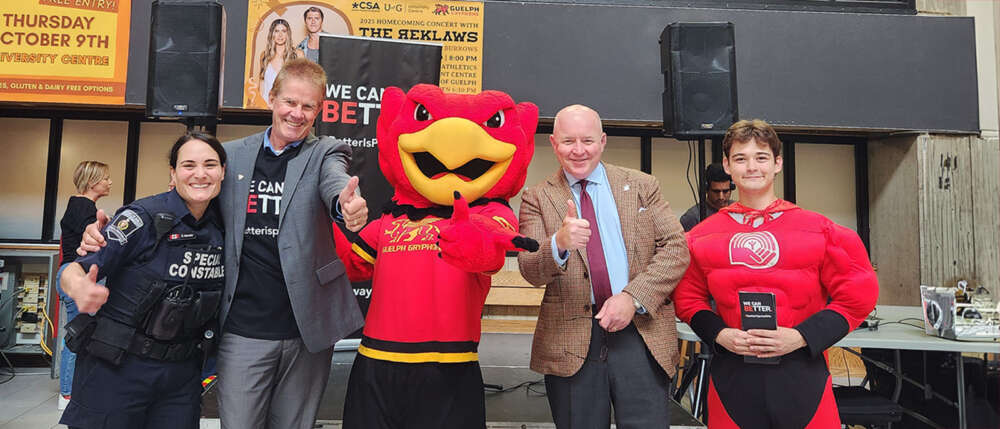 Four people stand around the Gryph mascot and give the thumbs up and smiles