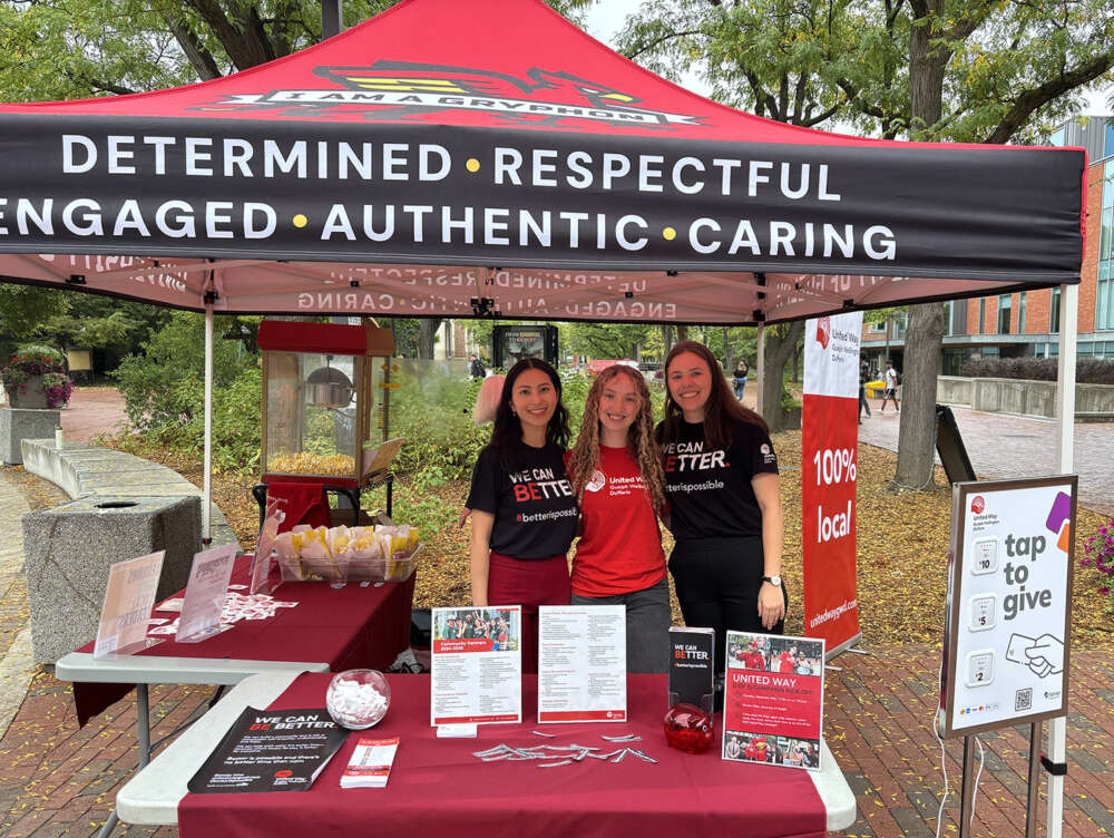 Three women wearing United Way t-shirts post for a photo at a United Way booth under a folding tent outside