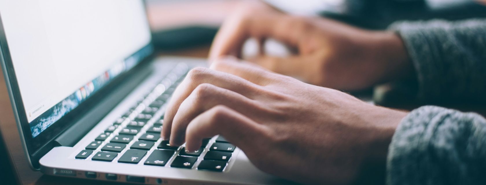 Close-up of hands typing on a silver Macbook