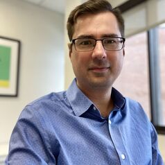 a person in a blue shirt and glasses poses for a headshot