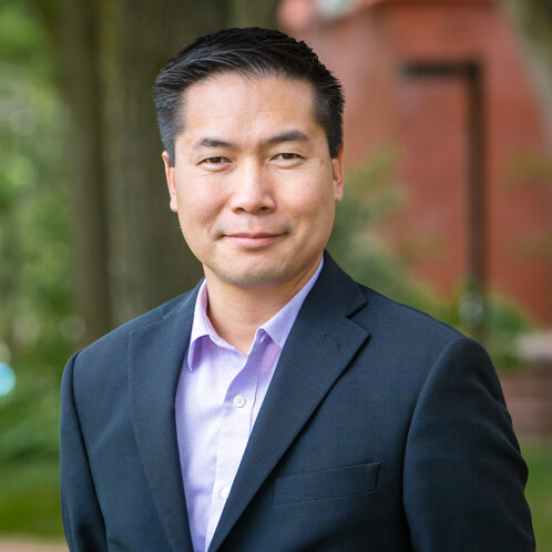 Person with short black hair poses in a suit