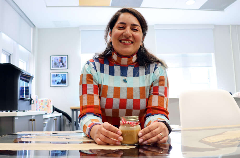 person sits at a glass table holding a mason jar with brown liquid