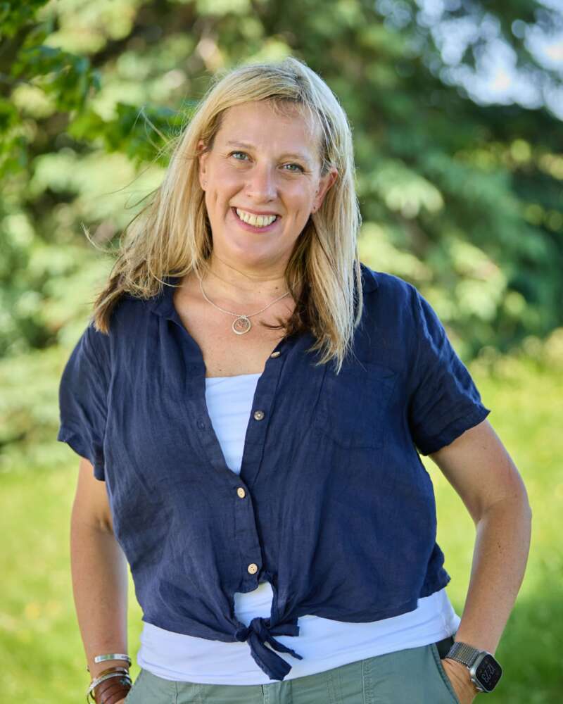 Kari Dunfield, with shoulder-length blond hair, smiles against greenery on bright day