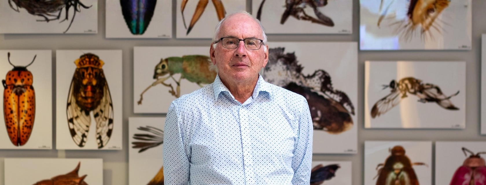Dr. Paul Hebert poses for a portrait in the atrium of the Centre for Biodiversity Genomics at the University of Guelph with canvas prints of magnified photos of insects hanging on the wall behind him